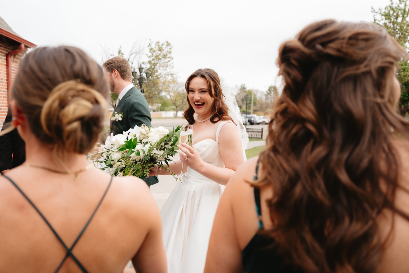 Bride holding champagne and laughing with bridesmaids after wedding ceremony